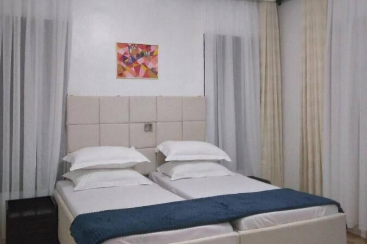 A hotel room with a large bed, white bedding, a blue throw blanket, and a ceiling light fixture.