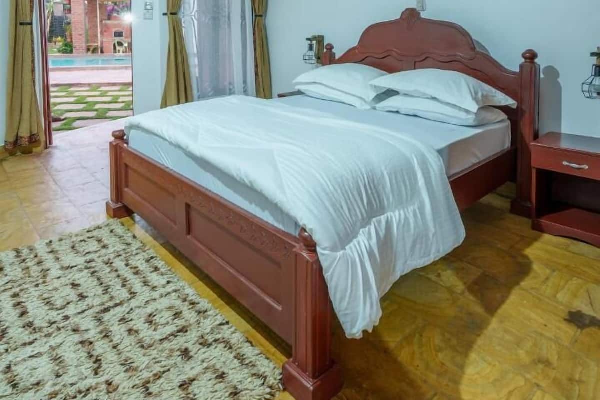 A bedroom with a wooden bed, a bedside table, and a view of the outside.