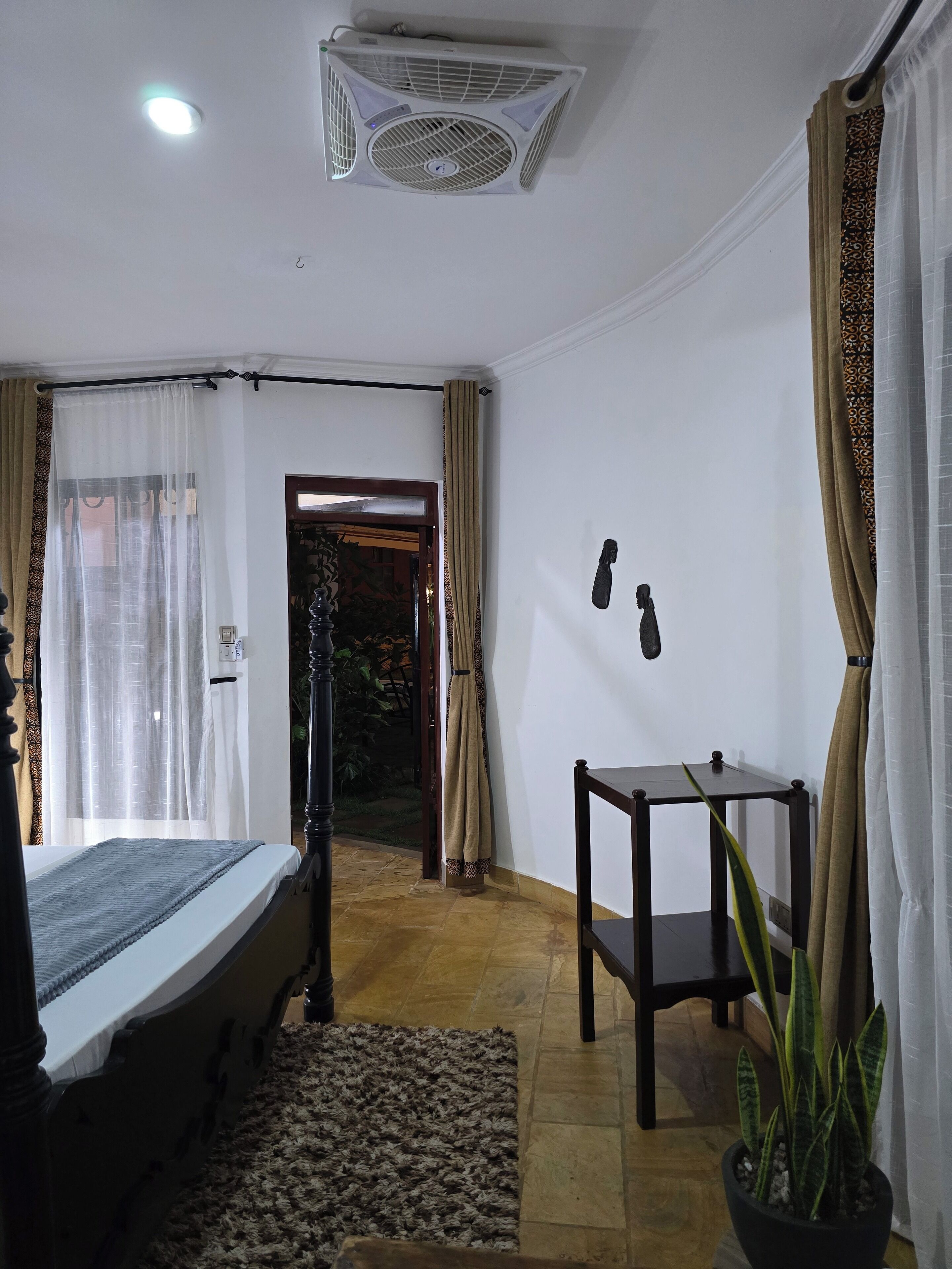 A room with a bed, a small table, a potted plant, and a ceiling fan.