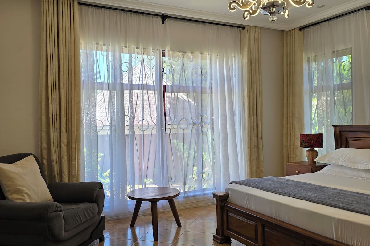 A bedroom with a large bed, a sitting area with a chair, a small round table, and a chandelier.