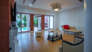 A spacious living room with a wooden floor, a sofa, a coffee table, and a television mounted on a brick wall. - Sprunger Avenue-Tulia Homes  (Moshi)