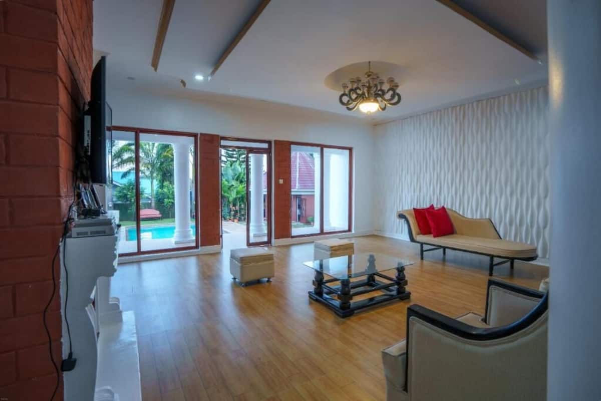 A spacious living room with a wooden floor, a sofa, a coffee table, and a television mounted on a brick wall.