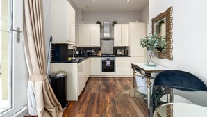A modern kitchen with white cabinets, a stainless steel range hood, and a glass dining table. - GuestReady - Fabulous stay in Fulham (London)