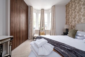 A hotel room with a large bed, a wooden wardrobe, a desk, and a chair. - GuestReady - Fabulous stay in Fulham (London)