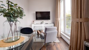 A modern living room with a glass coffee table, a flat-screen TV, a white console table, and a large window with curtains. - GuestReady - Fabulous stay in Fulham (London)