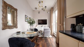 A modern kitchen with a round dining table, a black chair, a vase with green plants, a TV, and a coffee machine. - GuestReady - Fabulous stay in Fulham (London)