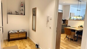 Een modern appartement met een houten vloer, een bankje met gestreepte kussens, een spiegel, een telefoon en een keukenhoek met een eettafel en stoelen.