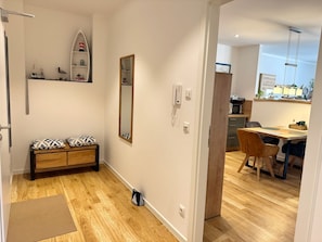 Um apartamento moderno com piso de madeira, um banco com almofadas estampadas, um espelho, um telefone e uma cozinha com mesa e cadeiras.