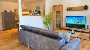 Een moderne woonkamer met een grijze bank, een houten kast en een tv waarop geanimeerde personages te zien zijn.