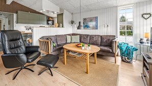 A modern living room with a sectional sofa, a black leather chair, a wooden coffee table, and a kitchen in the background.