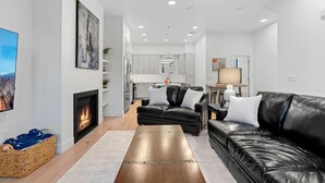 Una sala de estar moderna con chimenea, sofás de cuero negro y una cocina al fondo.