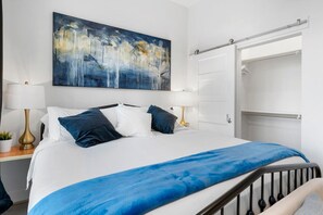 Une chambre d’hôtel avec un grand lit, un tableau au mur, une armoire et une table de chevet avec une lampe.