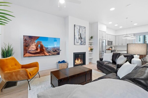 Un salon moderne avec une cheminée, un grand tableau et une cuisine en arrière-plan.