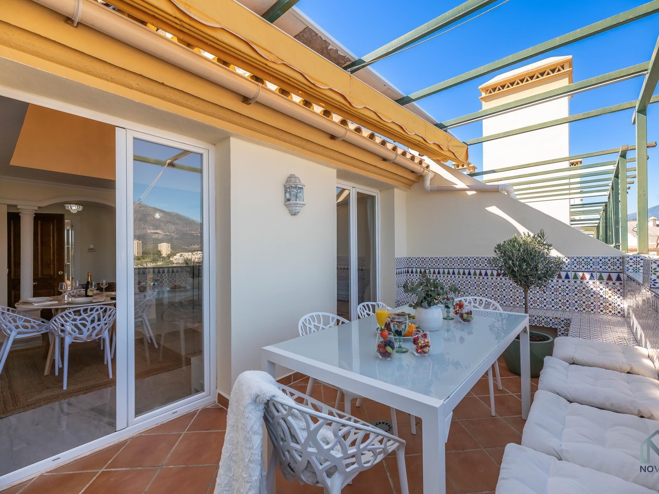 Un patio al aire libre con una mesa lista para comer, rodeado de sillas blancas.