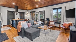 A spacious living area with a grey sectional sofa, a wooden coffee table, and a kitchen in the background.