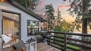 An outdoor deck with a grill, seating area, and a view of trees and a sunset.