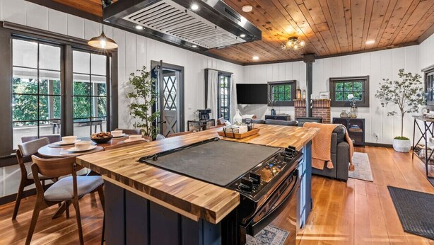 A modern kitchen with a central island, wooden flooring, and large windows.