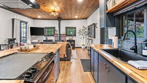 A modern kitchen with a central island, wooden ceiling, and large windows.