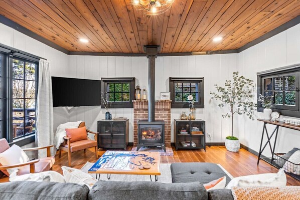 Una sala de estar acogedora con chimenea, techo de madera y ventanas amplias.