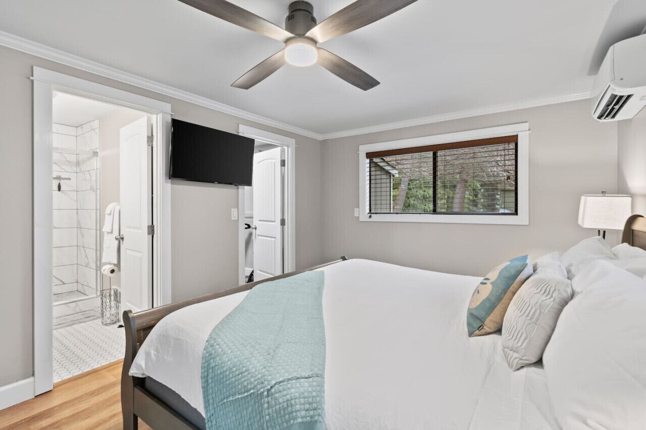 Une chambre à coucher comprenant un lit, un ventilateur de plafond, une télévision, une fenêtre avec vue et une porte donnant sur une salle de bain.