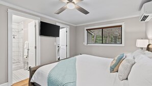 Ein Schlafzimmer mit Bett, Deckenventilator, Fernseher, Fenster mit Blick und einer Tür zu einem Badezimmer.
