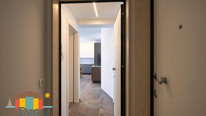 Un corridoio conduce a una cucina dal design moderno, con una maniglia della porta ben visibile e un logo nell'angolo in basso a sinistra.