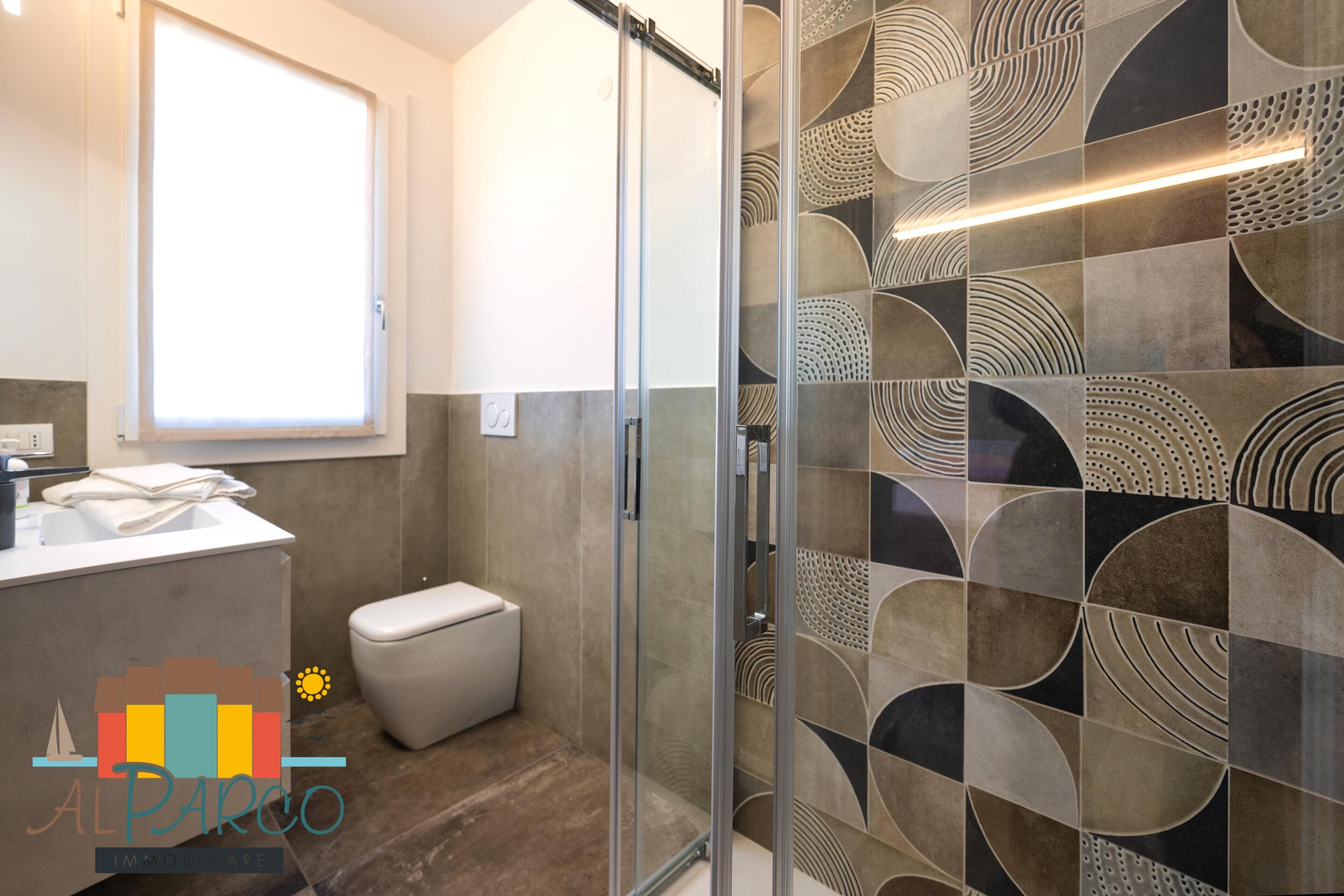A modern bathroom with a glass shower enclosure, a toilet, and a sink with a towel.