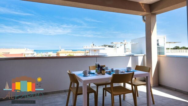 Un balcone con un tavolo apparecchiato per due, affacciato su una veduta panoramica della città e del mare.