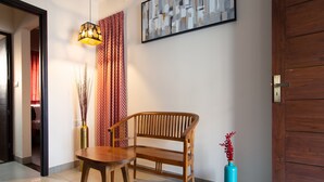 A modern living room with a wooden bench, a round table, a vase with red flowers, and a painting on the wall. - Sarvam Serviced Apartment (Coimbatore)