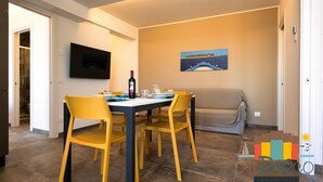 A dining area with a table set for four, yellow chairs, a flat-screen TV mounted on the wall, and a painting above the table. - Fantastic new penthouse with seaview P 21 (Rosolina Mare)