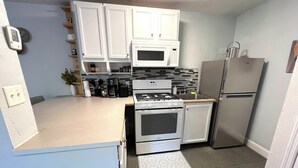 A compact kitchen with white cabinets, a built-in microwave, a gas stove, a refrigerator, and a coffee maker.