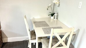 A dining area with a white table and chairs, a small potted plant, and a white wall with an electrical outlet.