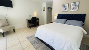 A hotel room with a bed, a desk, a chair, a TV mounted on the wall, and two framed pictures on the wall.