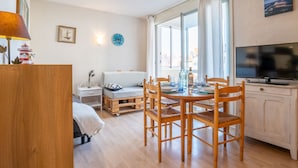 Une pièce chaleureuse avec une table à manger en bois, des chaises, un canapé, un téléviseur et une fenêtre avec des rideaux.