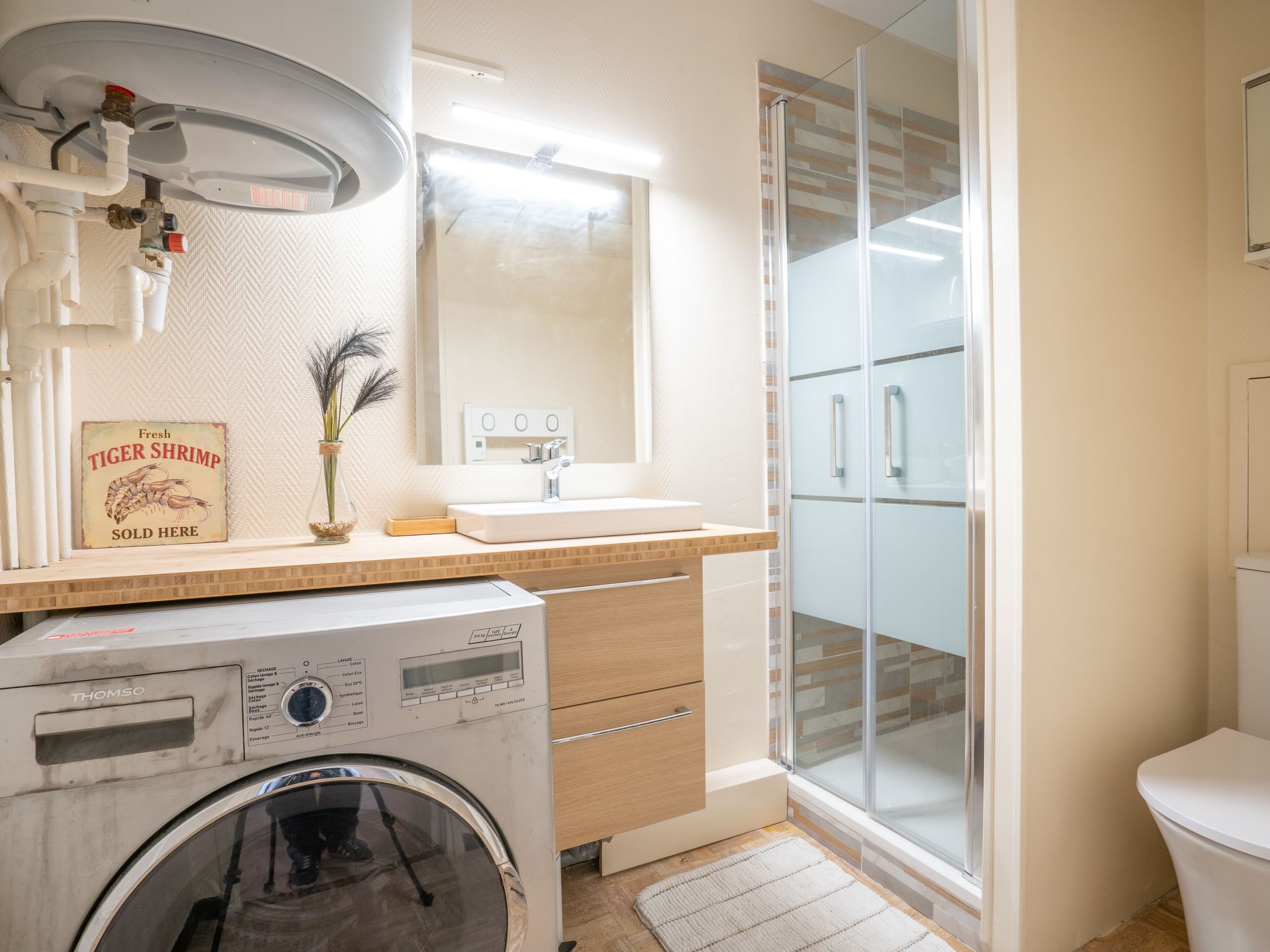 A modern bathroom with a washing machine, a sink, and a glass shower enclosure.