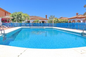 Une piscine d’un bleu éclatant, entourée d’une clôture bleue, avec une terrasse carrelée et des chaises longues.