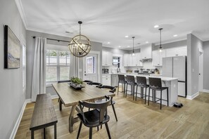 Una cocina moderna con armarios blancos, una mesa de comedor de madera y una isla grande con taburetes de bar.