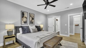 Ein modernes Schlafzimmer mit Bett, Nachttischen, einer Bank, Deckenventilator und Kunstwerken an den Wänden.