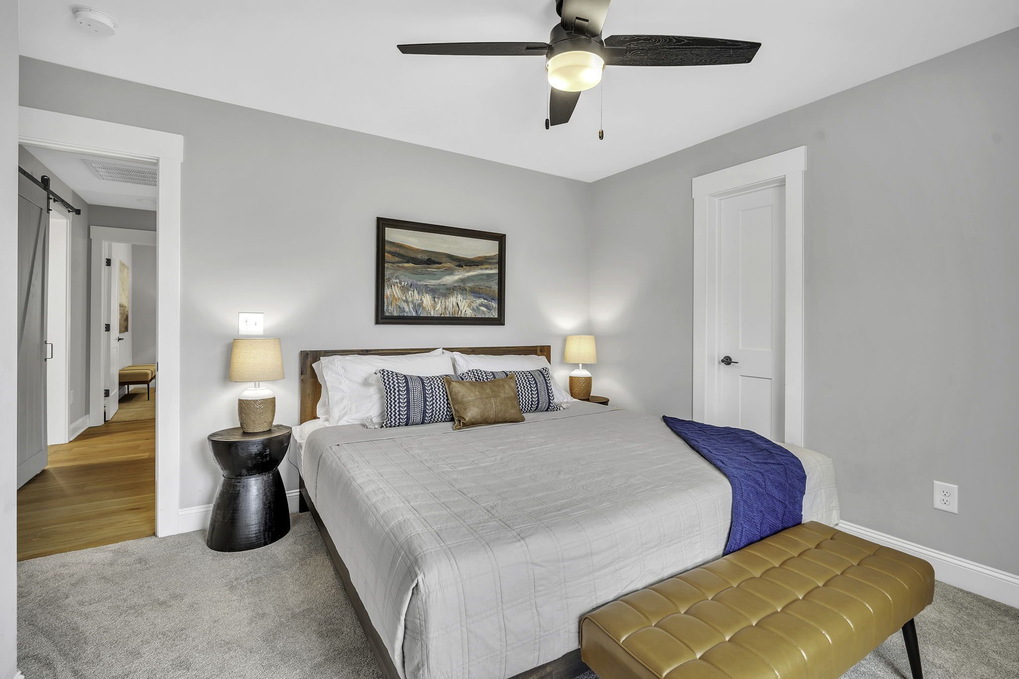 A bedroom with a bed, bedside lamps, a ceiling fan, and a painting on the wall.