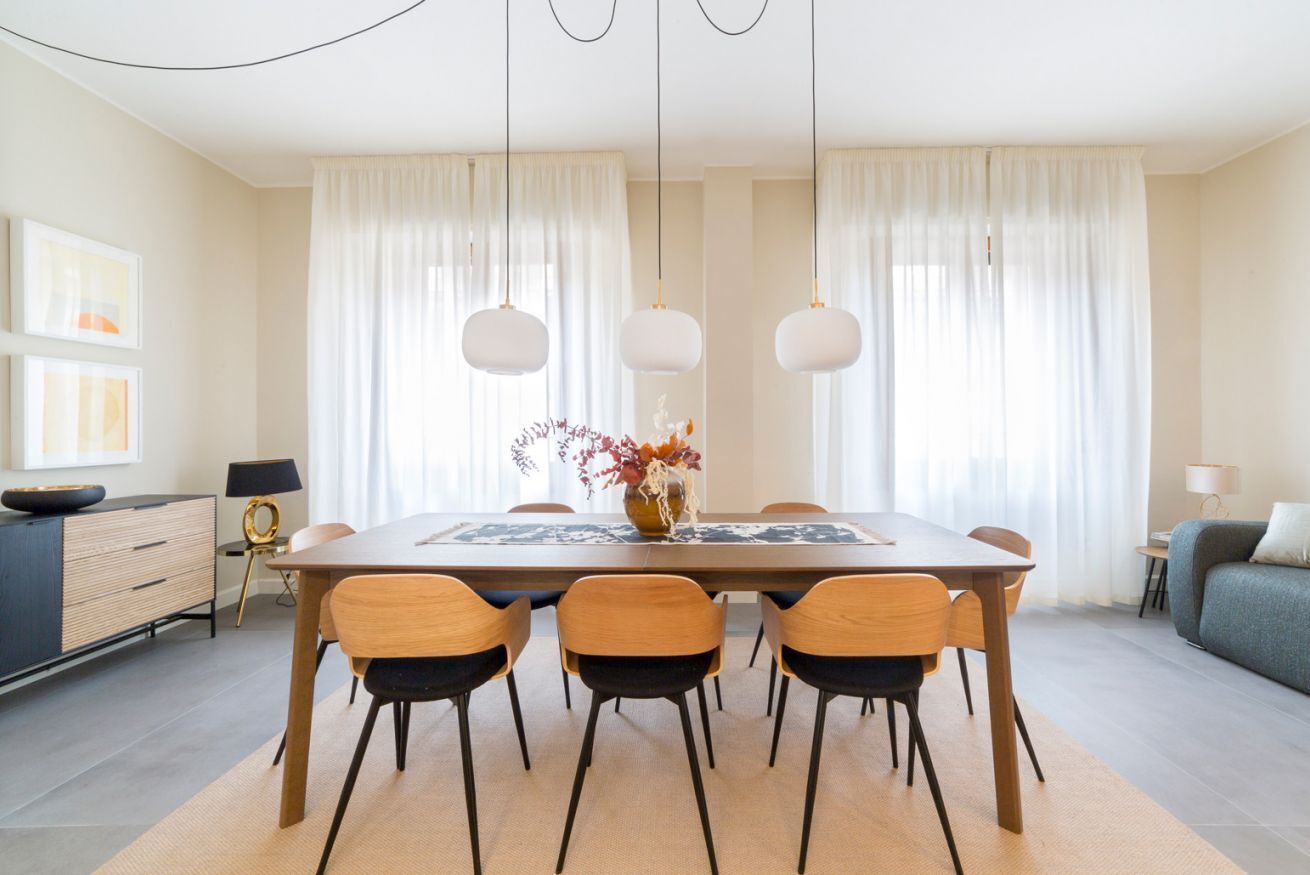A dining area with a wooden table, six chairs, a vase with flowers, and pendant lights.