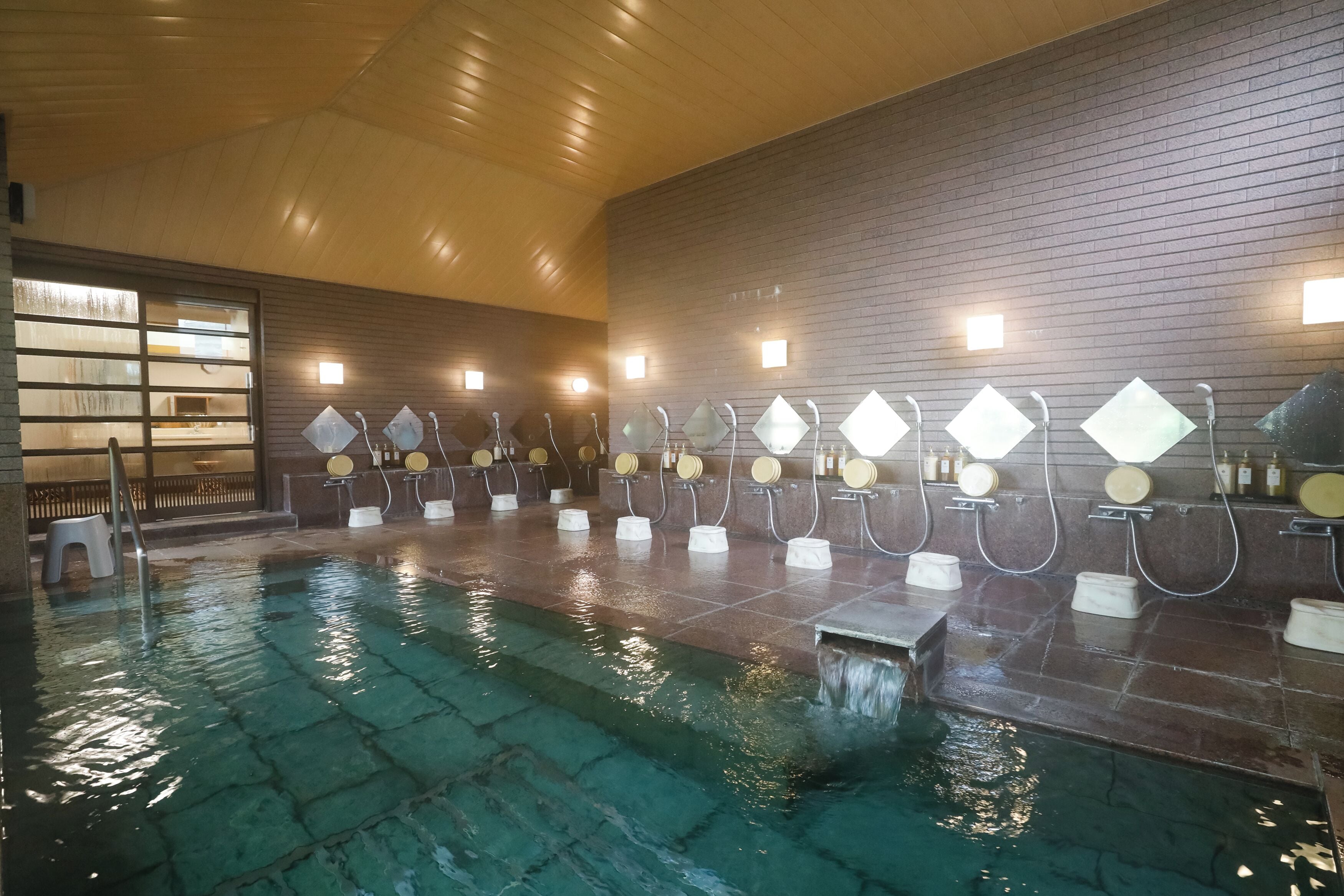 A spa area with a large indoor pool, multiple shower stations, and a wooden ceiling.