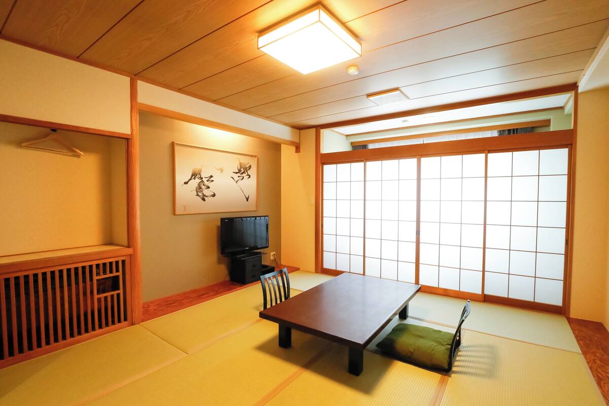 A traditional Japanese room with tatami flooring, a low table, a chair, a television, and a shoji screen.