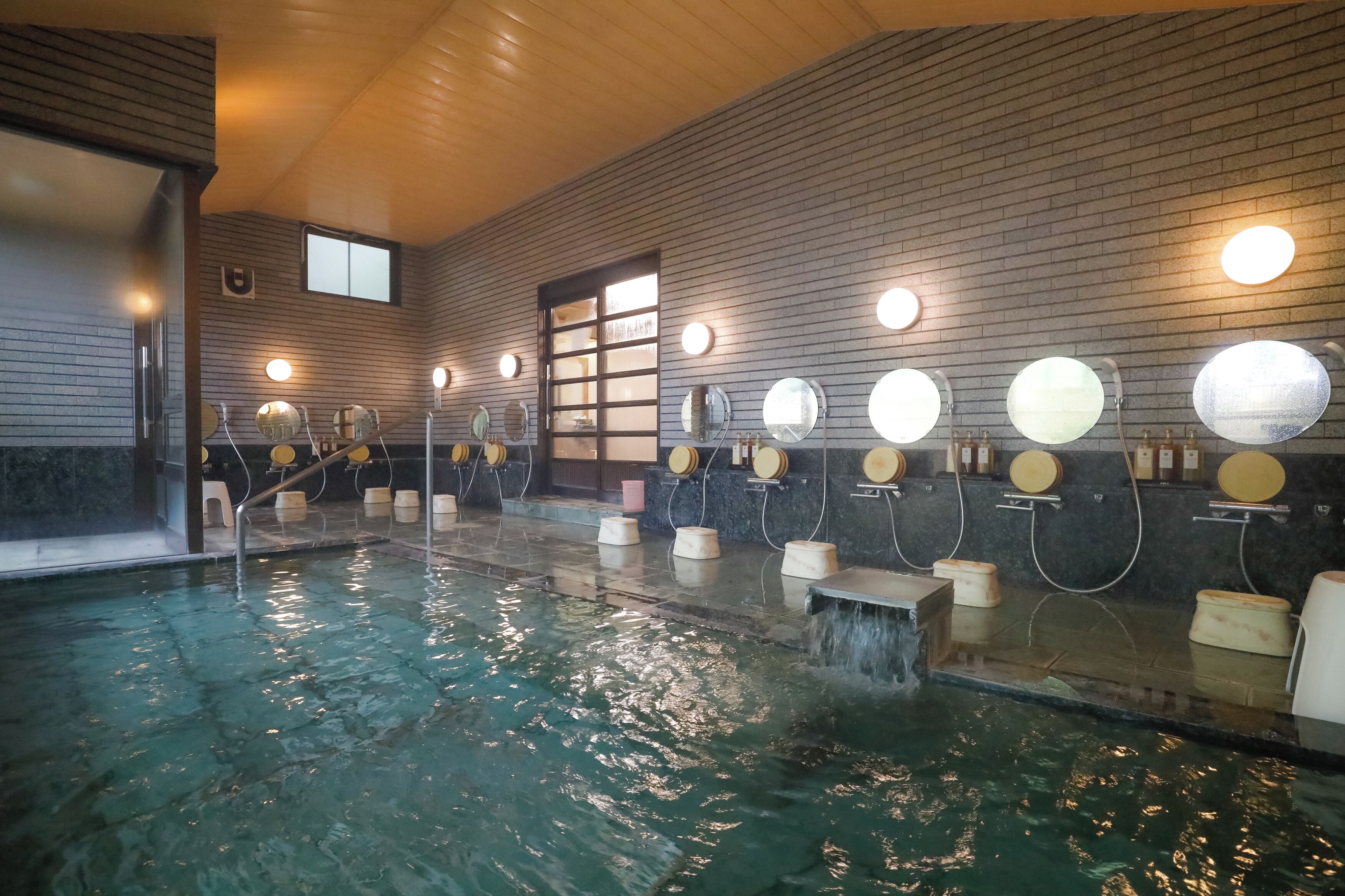 An indoor swimming pool with multiple mirrors and lights on the walls, a wooden ceiling, and a tiled floor.