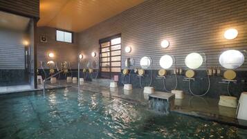 Una piscina interior con múltiples espejos e iluminación en las paredes, techo de madera y suelo de baldosas.