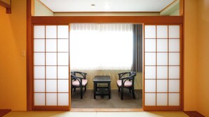 Una habitación japonesa tradicional con suelo de tatami, una puerta corredera shoji y una pequeña mesa con dos sillas.
