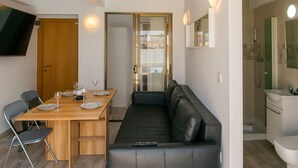 Un espacio habitable moderno con una mesa de comedor de madera, un sofá de cuero negro y un televisor montado en la pared.
