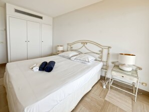 A hotel room with a bed, a wardrobe, a bedside table with a lamp, and a power outlet.