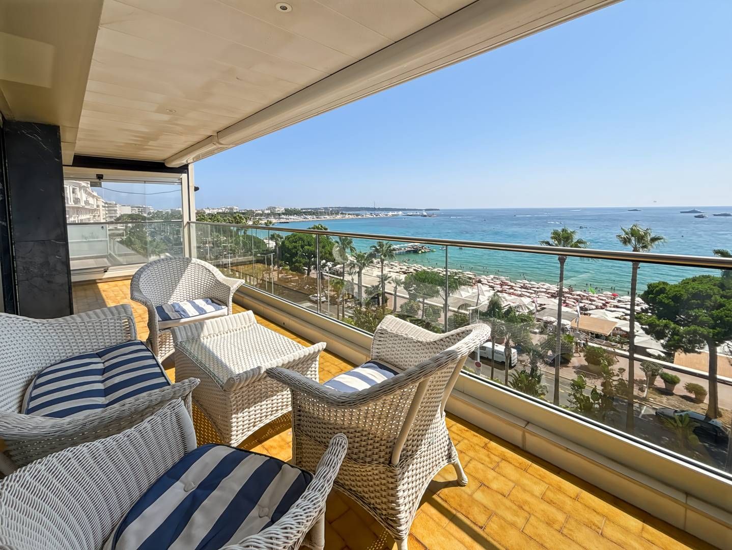 A balcony with wicker furniture and a view of the beach and sea.