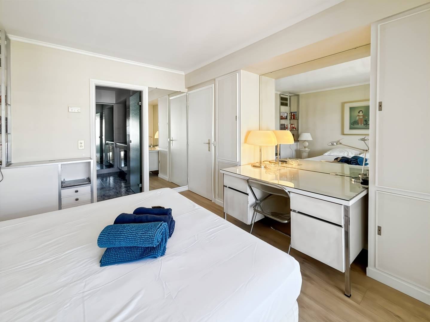 A hotel room with a bed, a desk, a chair, a mirror, and a bathroom visible through an open door.