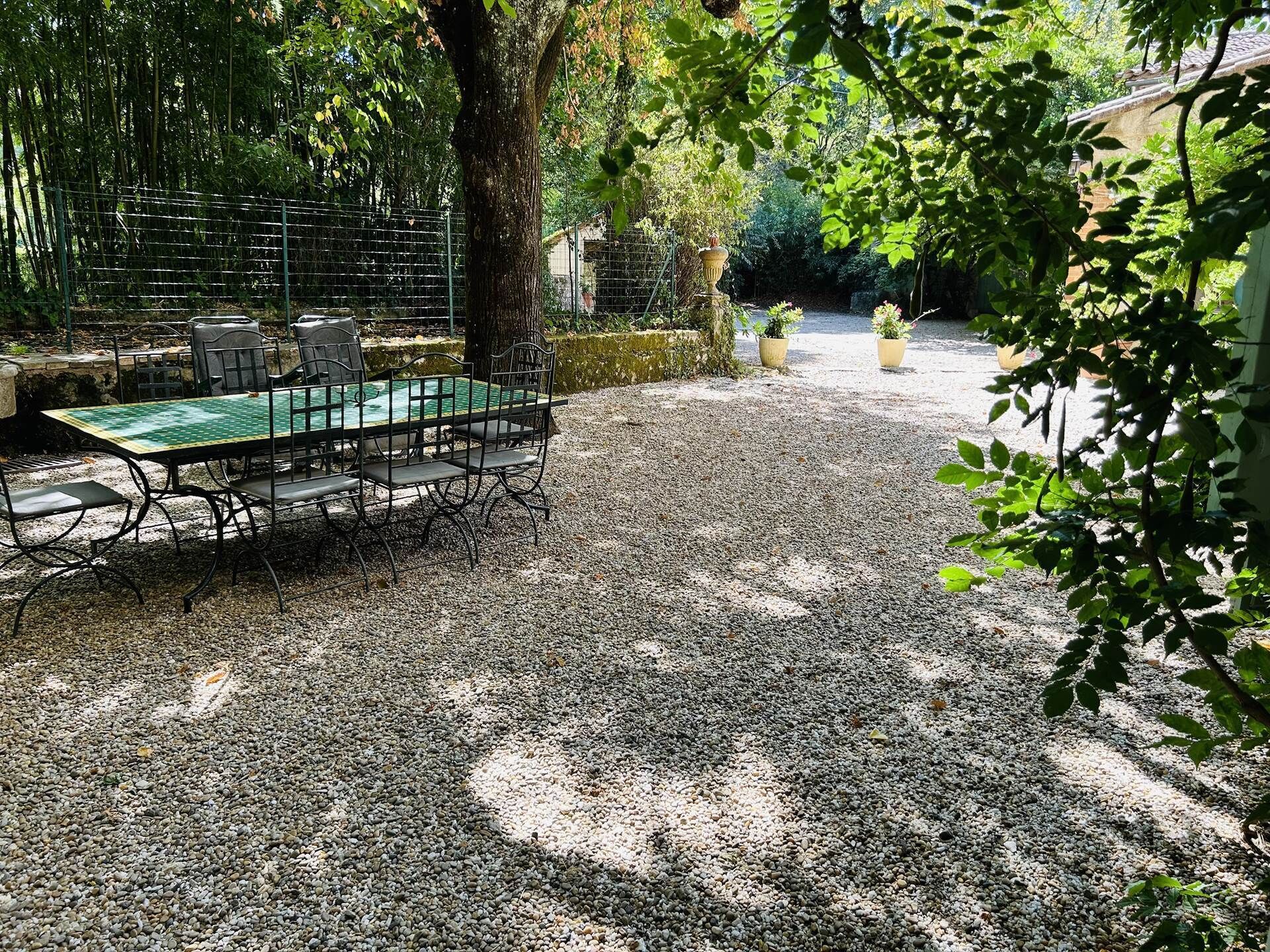 An outdoor dining area with a table and chairs, surrounded by gravel and greenery.